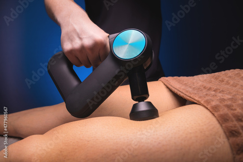 Close-up of a professional male masseur stimulates the leg muscles of a male patient in a dark spa room for massage. Percussion mechanical effect on overstrained muscles photo