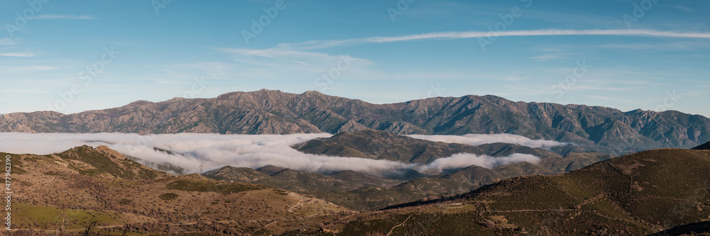 Panoramic view of low clouds hanging in a valley of a natural park in the balagne region of Corsica with mountains in the distance