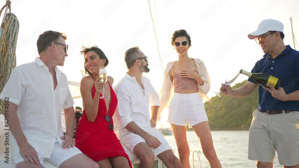 Group of man and woman friends enjoy party drinking champagne with talking together while catamaran boat sailing at summer sunset. Male and female relax outdoor lifestyle on tropical travel vacation Group of man and woman friends enjoy party drinking champagne with talking together while catamaran boat sailing at summer sunset. Male and female relax outdoor lifestyle on tropical travel vacation