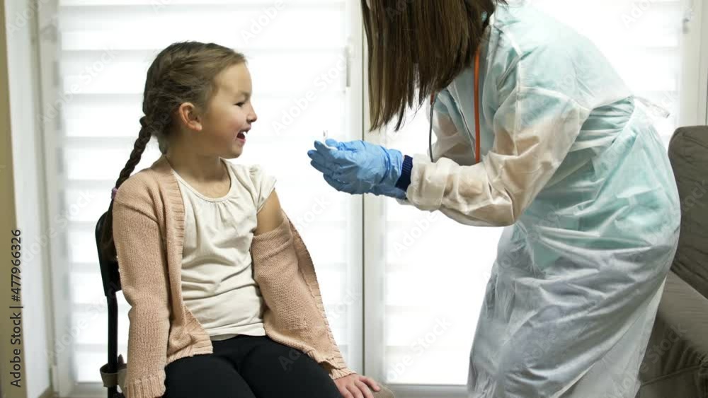 Female nurse in protective uniform and medical mask making covid-19 vaccine injection to girl 7-8 years old in clinic lab room, vaccination concept. Female nurse in protective uniform and medical mask making covid-19 vaccine injection to girl 7-8 years old in clinic lab room, vaccination concept.