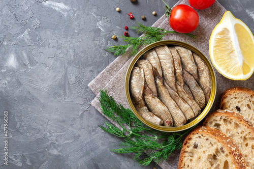 Smoked sardines in an open tin can, crispy whole grain bread, greens, lemon, fresh tomatoes ha concrete background with copy space. Top view, flat lay. photo