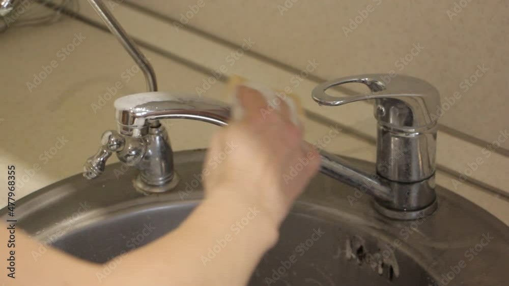 Chrome water tap faucet cleaning on stainless steel round kitchen sink with female white hand without glove closeup POV view Chrome water tap faucet cleaning on stainless steel round kitchen sink with female white hand without glove closeup POV view