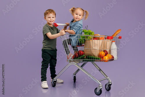 Little boy pushing a little girl inside a shopping cart. Isolated concept image..