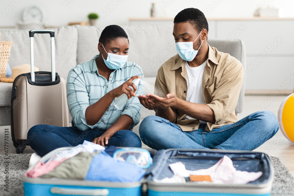 African Family Spraying Sanitizer Sitting With Travel Suitcase At Home African Family Spraying Sanitizer Sitting With Travel Suitcase At Home