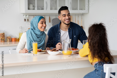 Happy Young Muslim Parents Looking At Little Daughter While Eating Breakfast Together