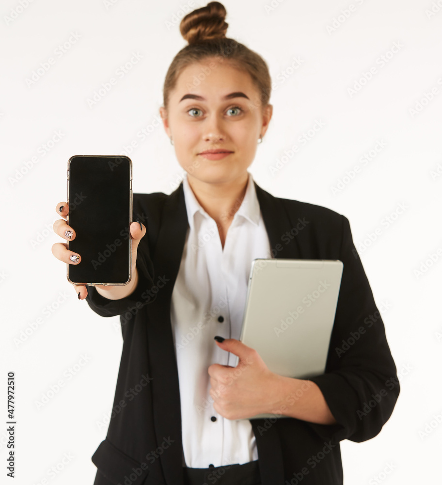 Naklejka premium A young girl in office clothes holds a phone in her hands and shows it to the viewer, while a tablet is in her other hand.