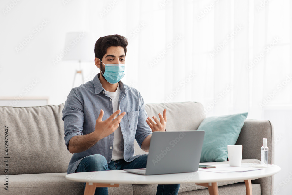 Online work with client remotely. Arab man in protective face mask having video call via laptop, working from home Online work with client remotely. Arab man in protective face mask having video call via laptop, working from home