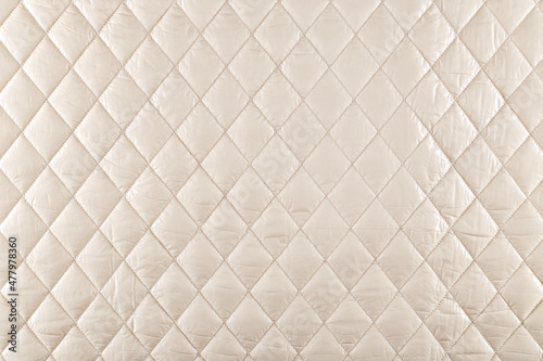 smooth surface of quilted jacket fabric of cream color, background, texture
