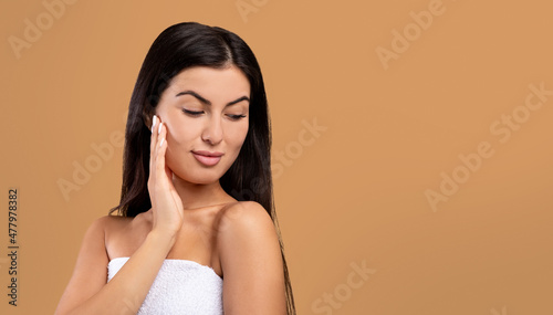 Spa facial concept. Beautiful armenian woman touching her soft skin, posing over brown background with copy space