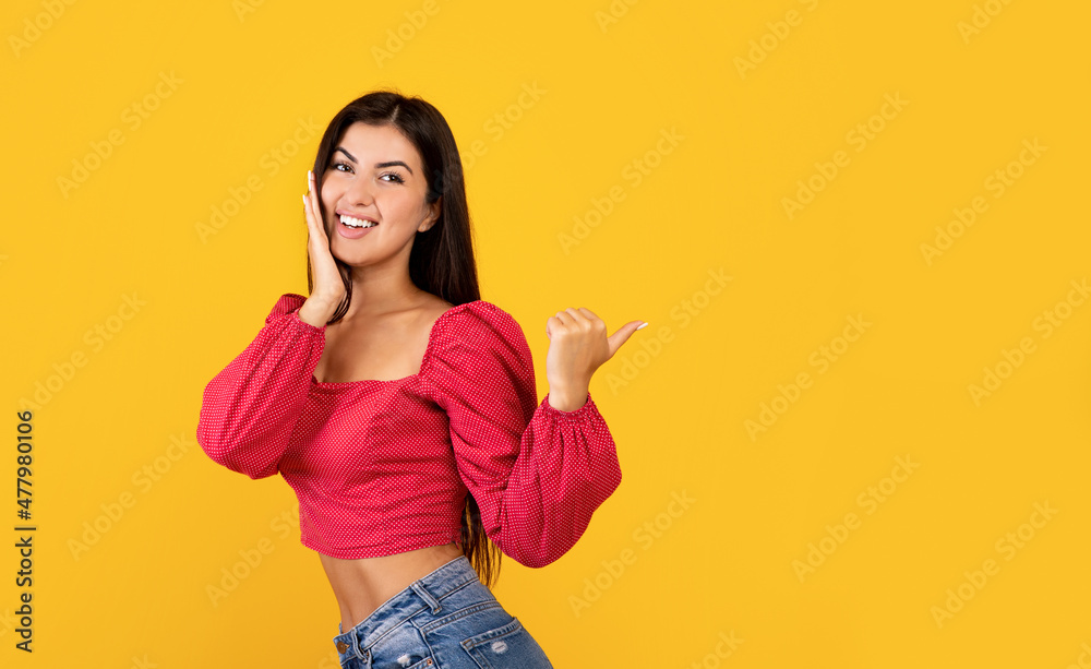 Wow, look here. Amazed armenian lady pointing at free space over yellow studio background, panorama Wow, look here. Amazed armenian lady pointing at free space over yellow studio background, panorama