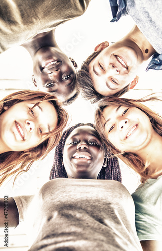 Upward view of teenagers smiling together in a circle. Multi ethnic friends happy, freindship and antiracism concept photo