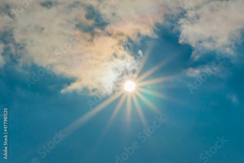 The sun in the blue sky under the clouds. Sunny day. Blue sky. Bright midday sun illuminates the space. Blue sky with clouds and sun reflection. The sun shines bright in the daytime in summer.