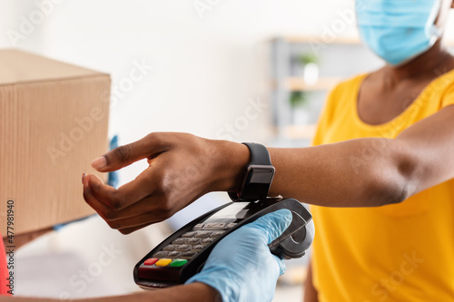 African Female Making Payment Using Smartwatch Receiving Parcel Indoors, Closeup
