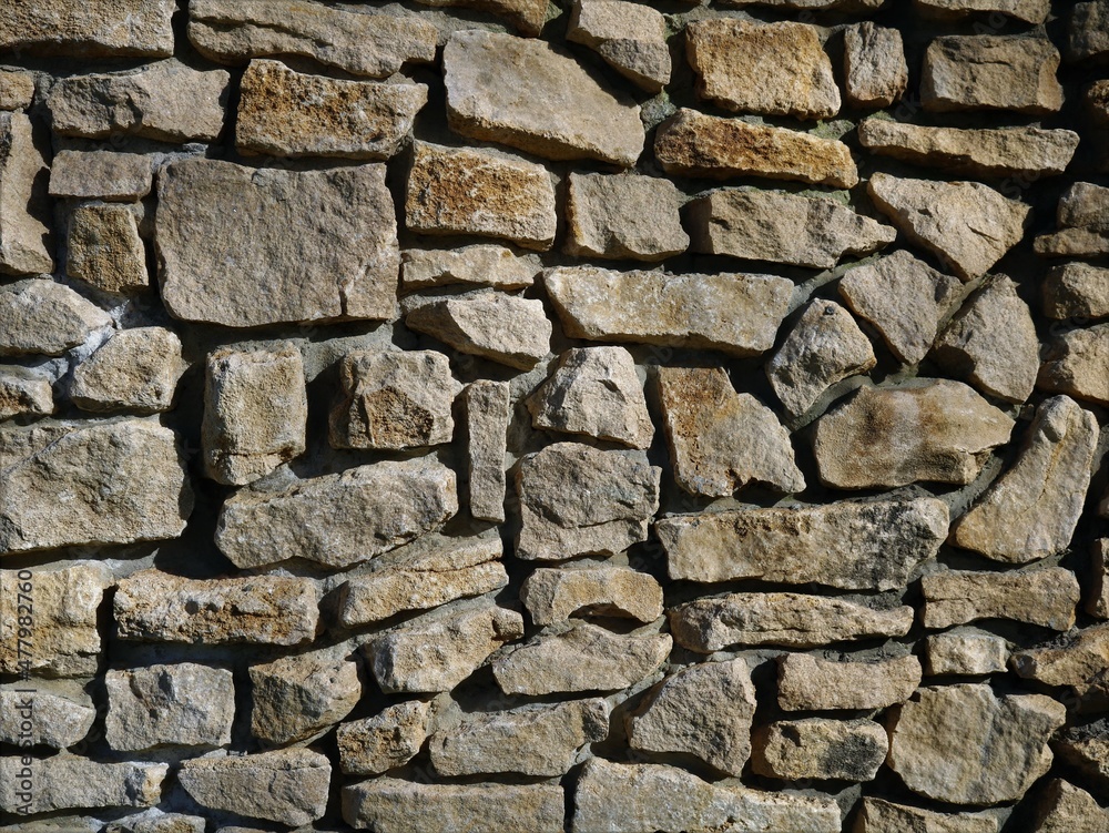 fragment of a stone wall with a rough texture of large masonry from natural rough cobblestones, solid stone texture in bright sunlight with detailing broken lines and chaotic irregularities fragment of a stone wall with a rough texture of large masonry from natural rough cobblestones, solid stone texture in bright sunlight with detailing broken lines and chaotic irregularities