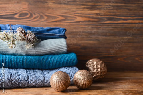 Stack of knitted sweaters and Christmas decor on wooden table, closeup