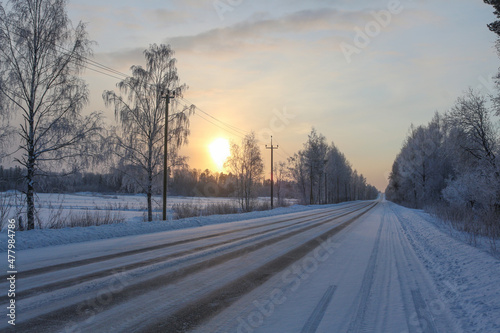 Winter road on a frosty day. Beautiful landscape with the sun in the haze and the trees in the snow © Alexander