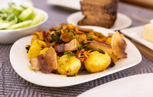 baked potatoes with chanterelles and bacon served with herbs on white plate