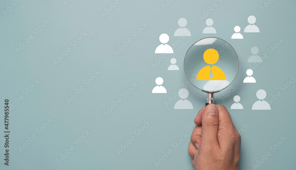 Hand holding magnifier glass and focus to manager icon which is among staff icons for human development recruitment leadership and customer target concept. - obrazy, fototapety, plakaty 