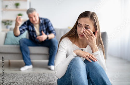 Mature man abusing his depressed wife, shouting, humiliating and threatening her, middle aged woman crying at home photo