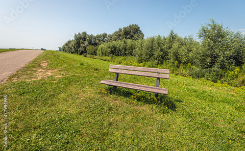 Inviting plastic bench in the grass of the roadside along a narrow country road. The photo was taken on a sunny summer day in the Dutch province of North Brabant.