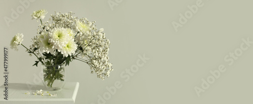 White chrysanthemums and gypsophila  flower in glass on gray interior. Selective soft focus. Minimalist still life. Light and shadow nature horizontal long background.