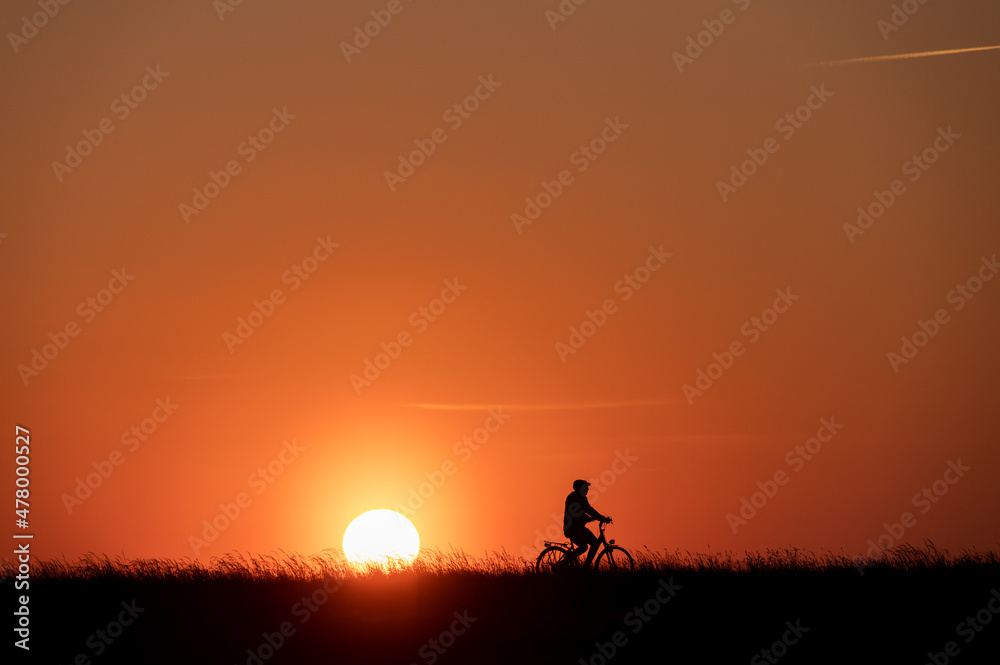 Silhouette of man on bike on grass on sunset with back lite and sun on backgound