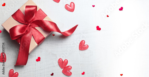 Top view photo of valentine's day decorations white gift box with red ribbon bow and small hearts on isolated light background.