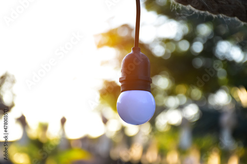 Bulb hanging on wire to decorate outdoor garden, sunlight and bokeh background.