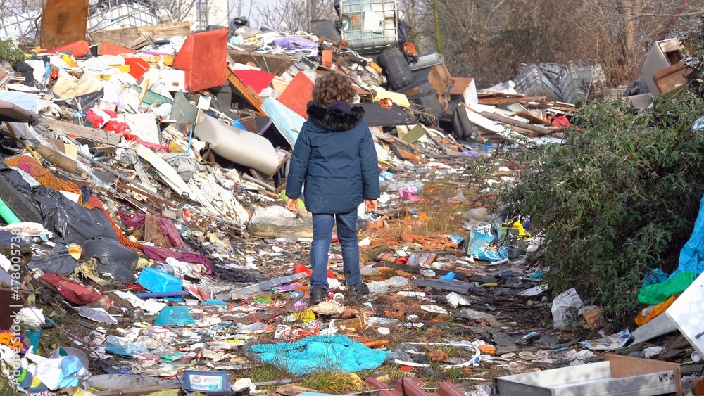 Europe, italy , Milan 7-year-old boy walks in the middle of an illegal and abusive landfill of polluting waste of various kinds - climate change, global warming and air pollution of the planet earth