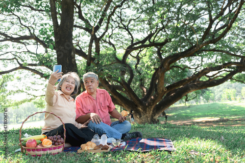 Asian elderly couple, husband and wife, Spent happy together, relaxing in the green garden, And using mobile phone to take a photo, concept to retirement aged couple on vacation with nature.