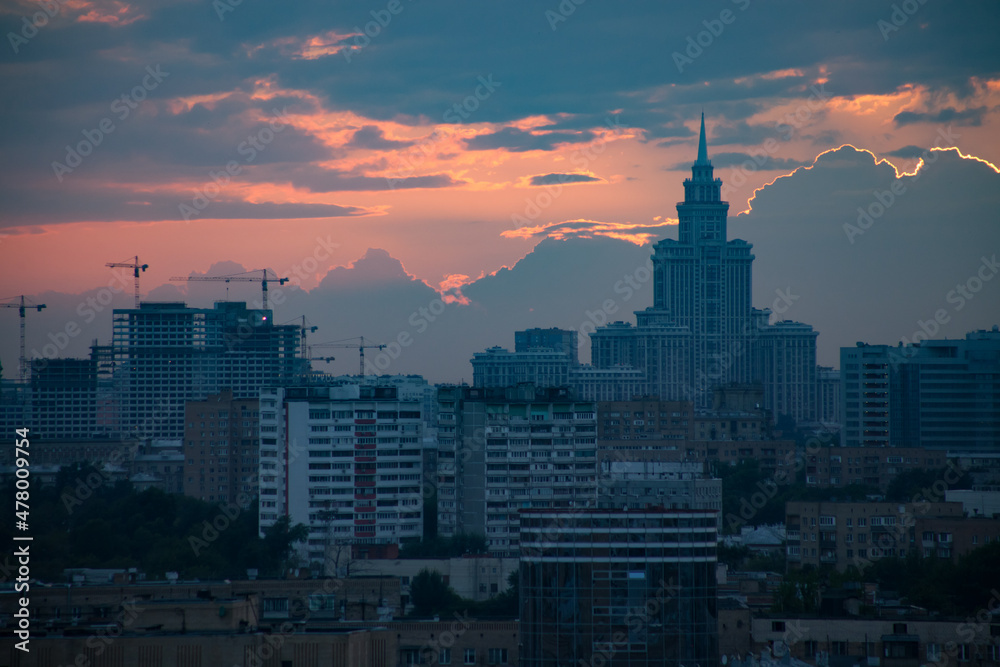 Fototapeta premium Pink and orange sunset with clouds and blue buildings and a cranes in the city. Moscow.