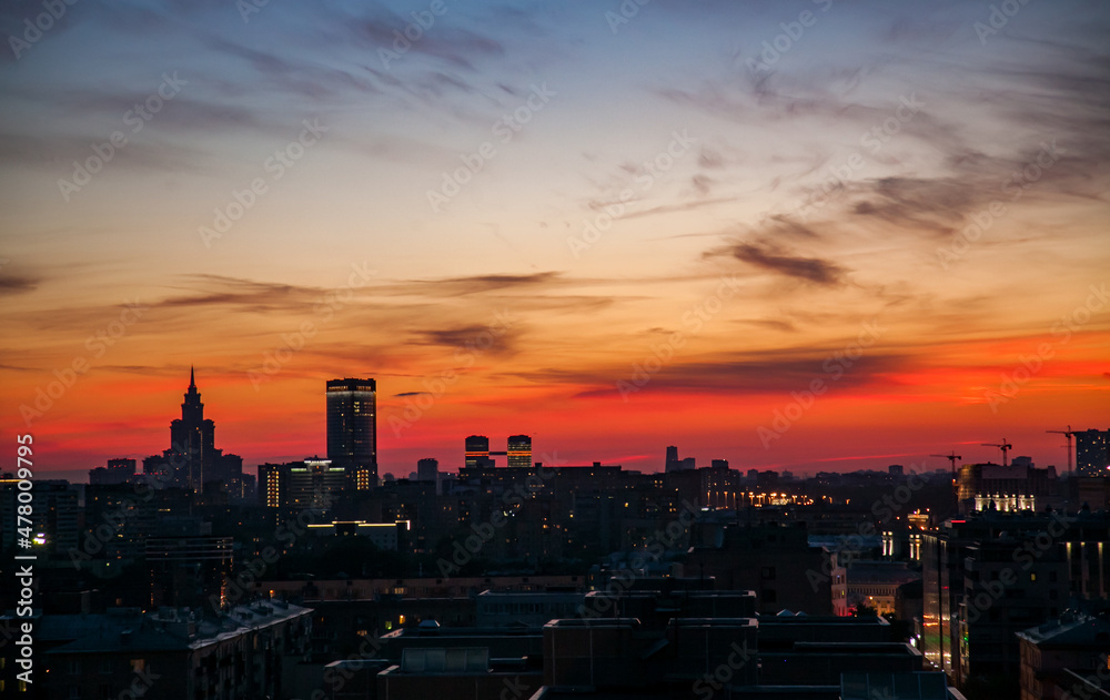 Red and blue sunset with clouds in the city. Silhouette of hi-rise buildings and cranes. Big city skyline. Moscow, Russia.
