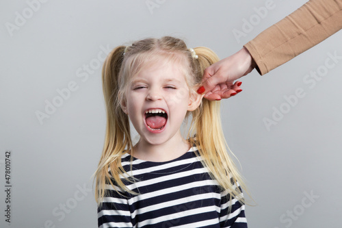 Disobedient little girl being punished by ear pulling, studio shot