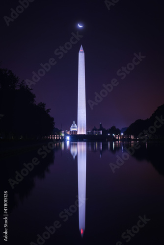 Washington DC monuments including the Capitol and Washington Monument as seen between columns of Lincoln Memorial at night with a crescent moon