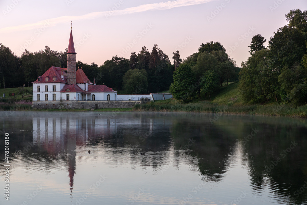 Prioratsky aka Priory palace in Gatchina stands on the shore of the pond. It is surrounded by a green forest. Small mansion, resembling a medieval 18th century European monastery with red tall spires.