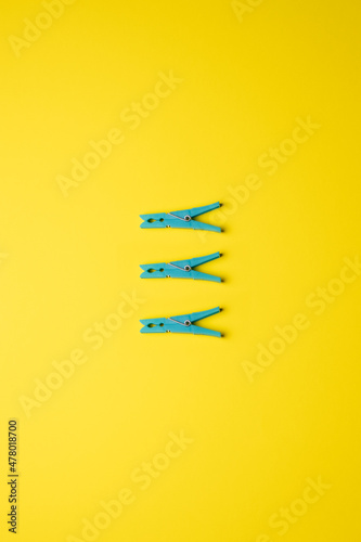 three blue clothespins centered and aligned vertically on a yellow background