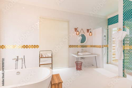 Luxury modern home bathroom interior with bright white cabinets, white marble decor, walk in shower, free tub. Luxurious hotel resort interior, elegant golden style design, green decoration bathtub