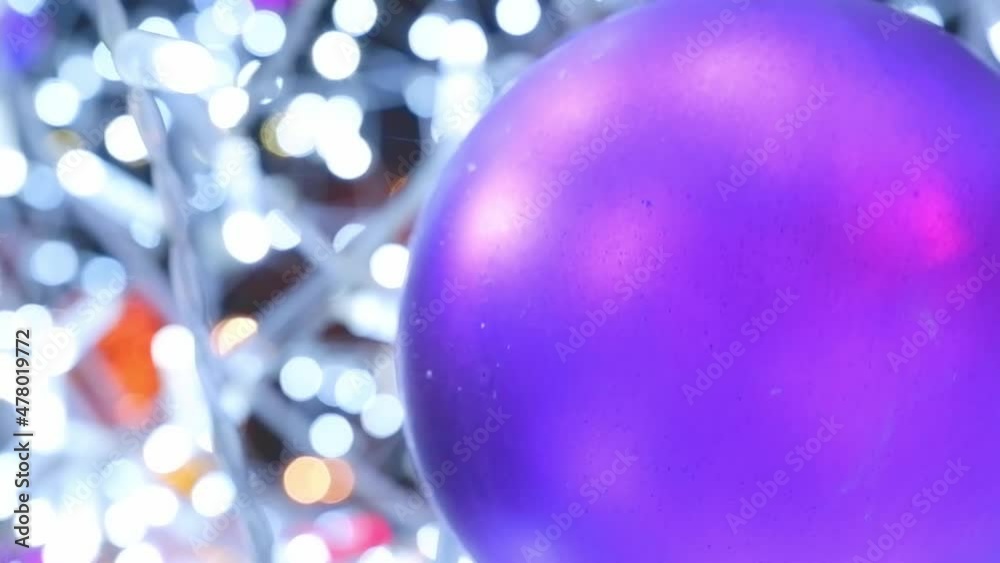 Happy New Year tree decorates a lilac glass ball on a snow branch against a background of bokeh side flickering garlands of light bulbs for a family holiday. Festive mood. Positive emotion.