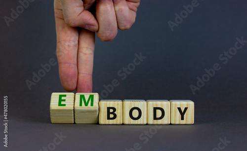 Body and embody symbol. Doctor turns wooden cubes and changes the concept word body to embody. Beautiful grey table, grey background, copy space. Medical, body and embody concept.