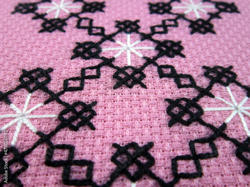      cross stitched pattern on pink fabric background close-up    