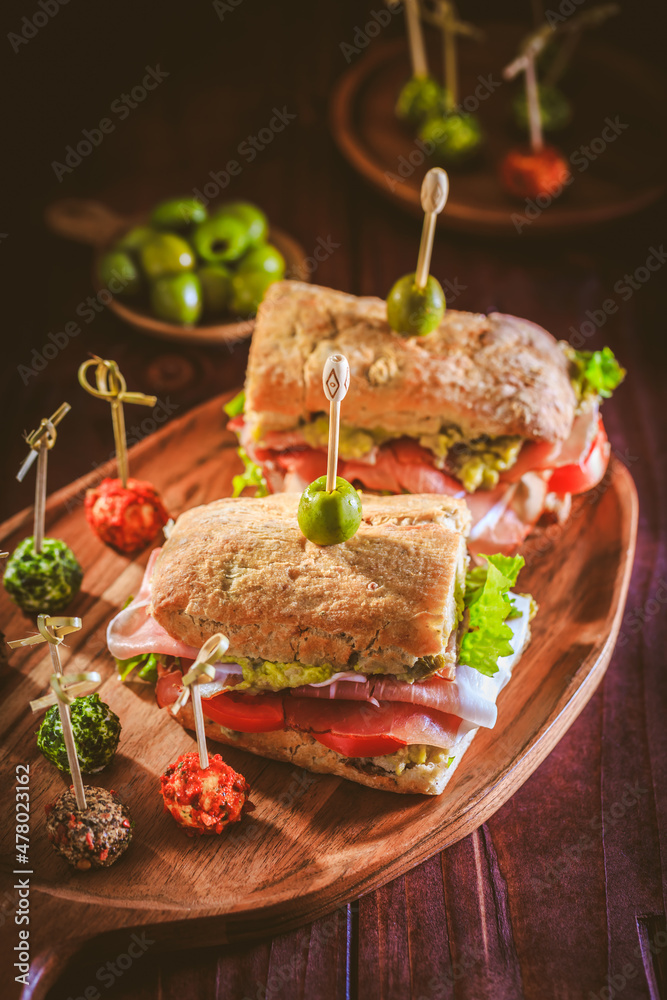 Ciabatta sandwich with guacamole, prosciutto, lettuce, tomato and olives