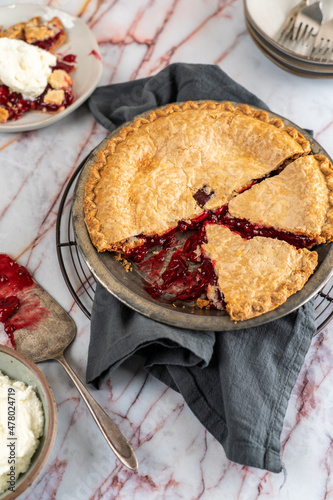 Sliced cherry pie in pie tin on cooling rack with ice cream