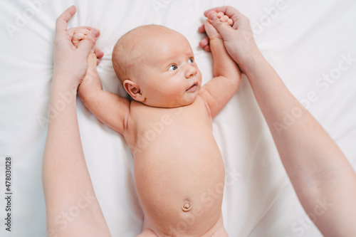 hands do exercises to baby on white sheet. gymnastics and massage for newborns.