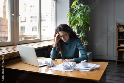 Stressed tired businesswoman exhausted overwhelmed at desk with laptop and crumpled paper. Frustrated girl journalist or entrepreneur suffer from lack of ideas for problem solution or creative crisis