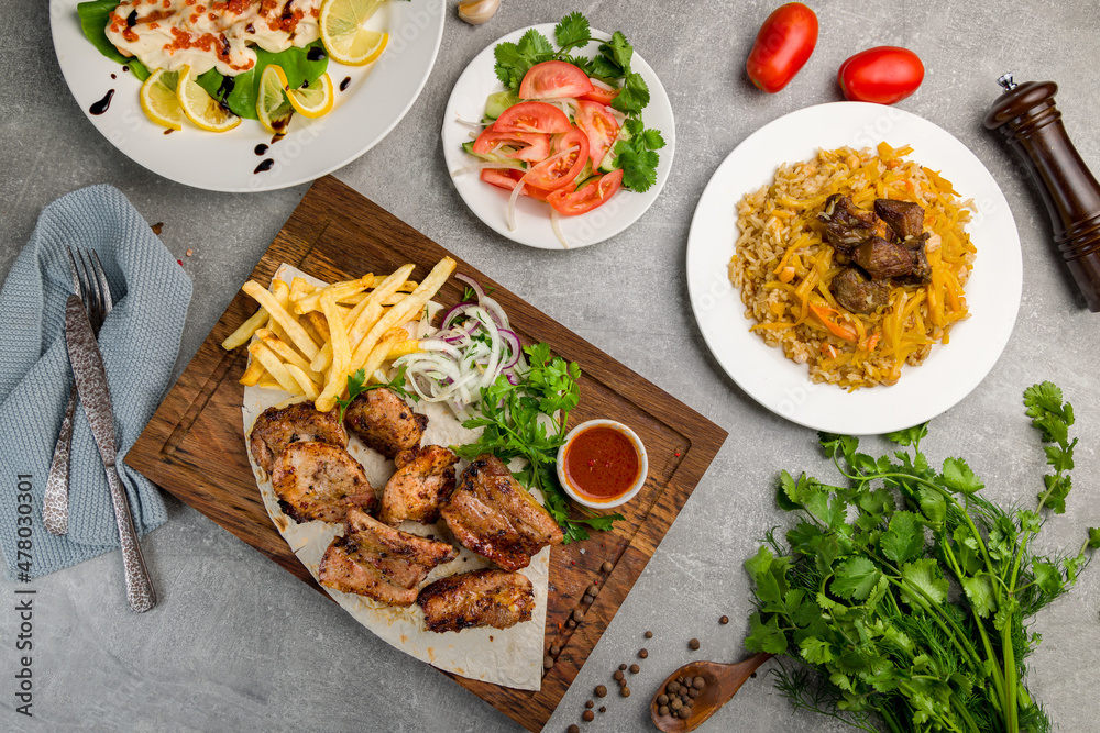 Kebab of pork, steak of salmon on creamy sauce with red caviar, vegetable salad and pilaf with beef top view on grey table Kebab of pork, steak of salmon on creamy sauce with red caviar, vegetable salad and pilaf with beef top view on grey table