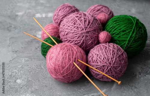 Bulk of pink, purple and green balls of yarn with knitting needles on grey background