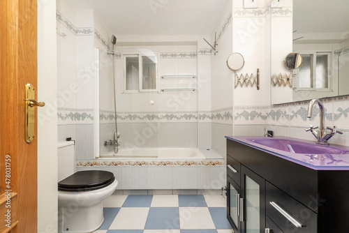 apartment toilet with dark cabinet under the mirror and bathtub with screen