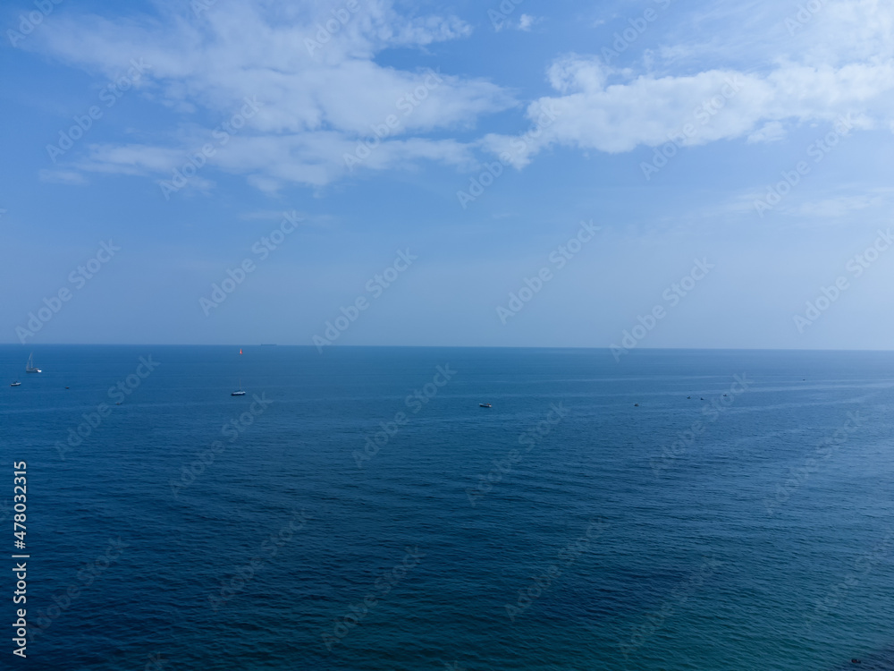 Blue horizon, where the cloudy sky and the blue sea converge. Ships and boats are barely visible on the water.
