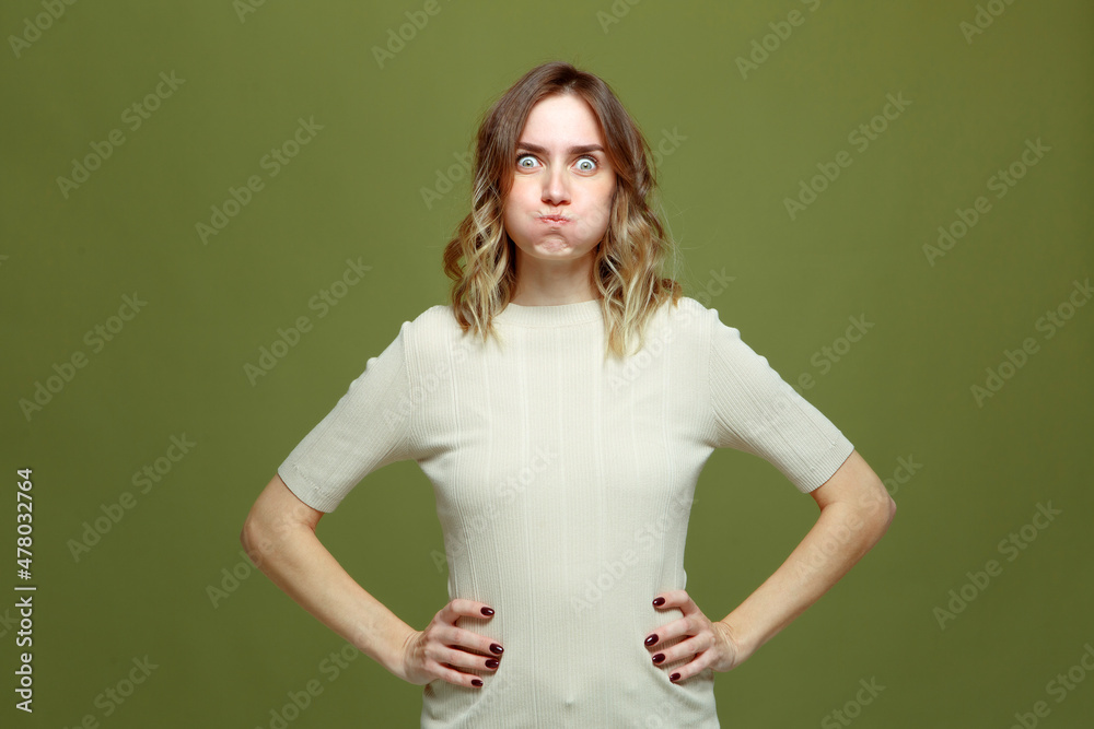 Funny comic young woman making faces puffed up her cheeks looking with big eyes at camera on green studio background Funny comic young woman making faces puffed up her cheeks looking with big eyes at camera on green studio background