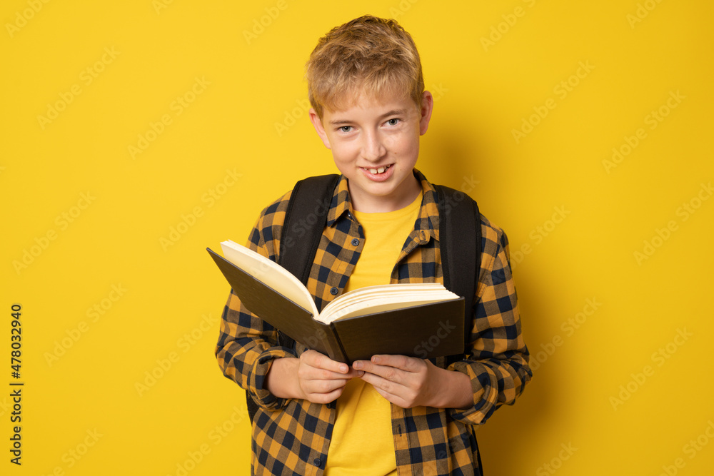 School boy wearing plaid shirt reading a book standing isolated over yellow background. School boy wearing plaid shirt reading a book standing isolated over yellow background.